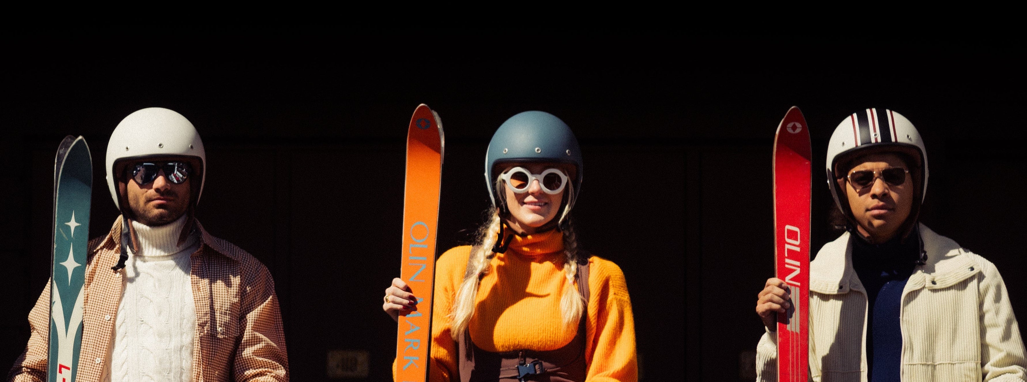 Four people with skis and helmets standing behind a wooden railing.